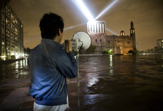 Voz Alta Persona de espaldas que sostiene un megáfono, de fondo el ministerio de Relaciones exteriores de México y sobre su techo tres haces de luces.